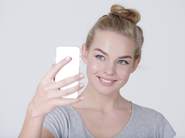 若い美しい白人の女の子は自分撮りをします。手に携帯電話を持つ幸せな素晴らしい女性