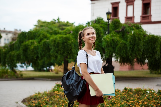 Foto gratuita giovane bella studentessa allegra che sorride, tenendo le cartelle all'aperto.