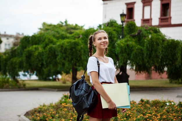 若い美しい陽気な女子学生笑顔、フォルダーを屋外に保持