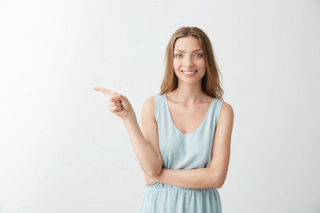 Free photo young beautiful cheerful girl smiling pointing finger in side over white backrgound.
