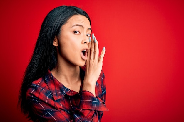 Free photo young beautiful chinese woman wearing casual shirt over isolated red background hand on mouth telling secret rumor whispering malicious talk conversation