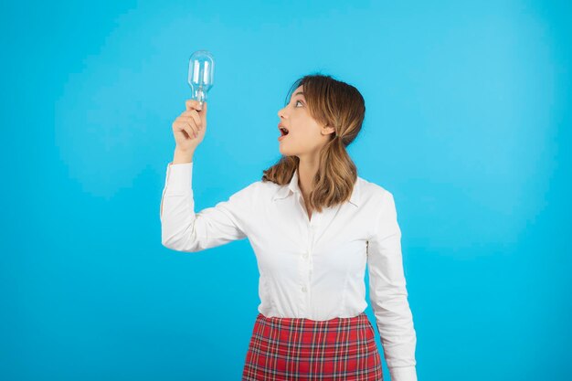 Young beautiful college girl holding idea bulb and looking at it with wide mouth. High quality photo