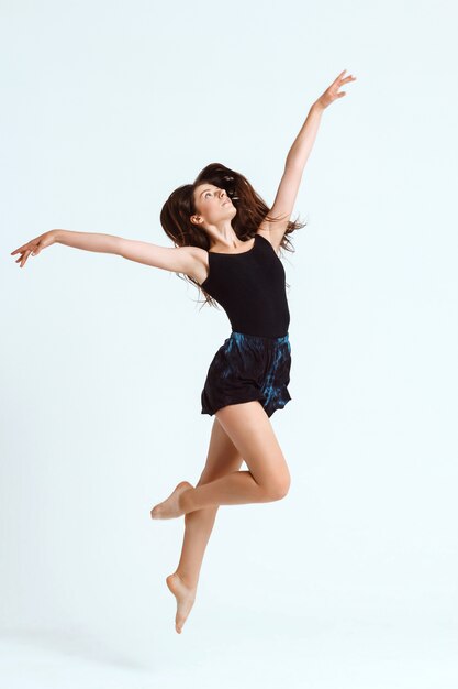 Young beautiful contemporary dancer posing over white wall. Copy space.