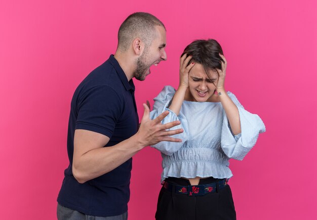 Young beautiful couple angry man shouting with aggressive expression at his confused girlfriend standing