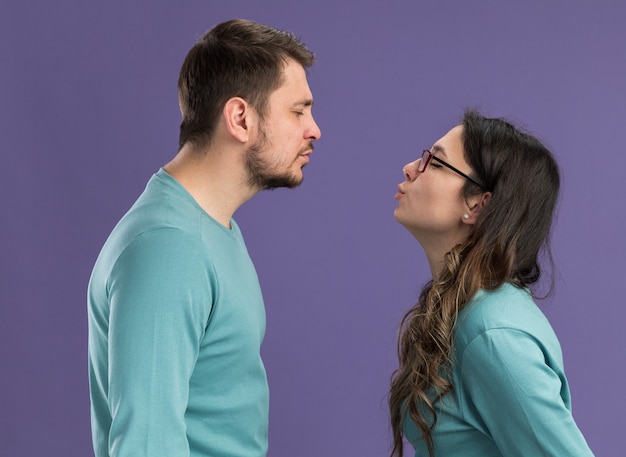Young beautiful couple in blue casual clothes happy and cheerful man and woman going to kiss happy in love standing over purple wall