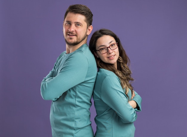 Young beautiful couple in blue casual clothes man and woman happy in love  standing back to back over purple wall