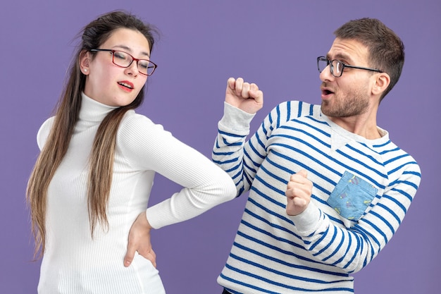 Foto gratuita giovane bella coppia in abiti casual uomo felice e donna divertirsi insieme per celebrare san valentino in piedi sul muro viola