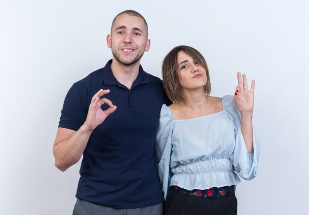 Young beautiful couple in casual clothes man and woman looking smiling cheerfully showing ok sign standing