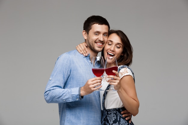 Young beautiful couple drinking wine, smiling over grey wall