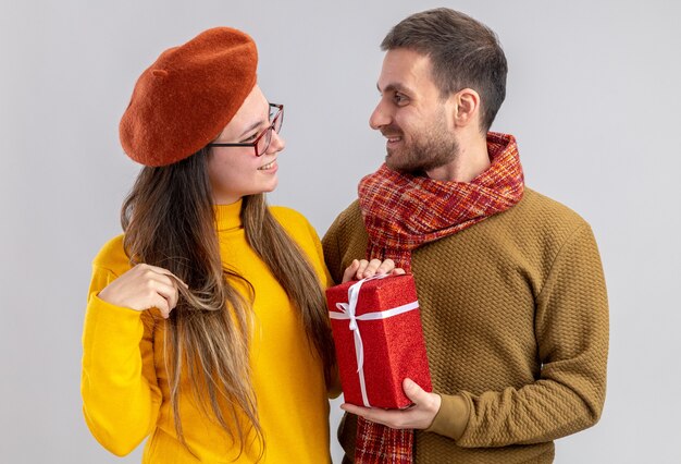 young beautiful couple happy man giving a present for his smiling girlfriend in beret happy in love together celebrating valentines day standing over white wall