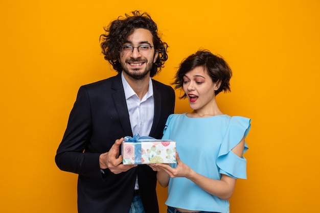 Young beautiful couple happy man giving a present to his surprised and amazed girlfriend celebrating valentine