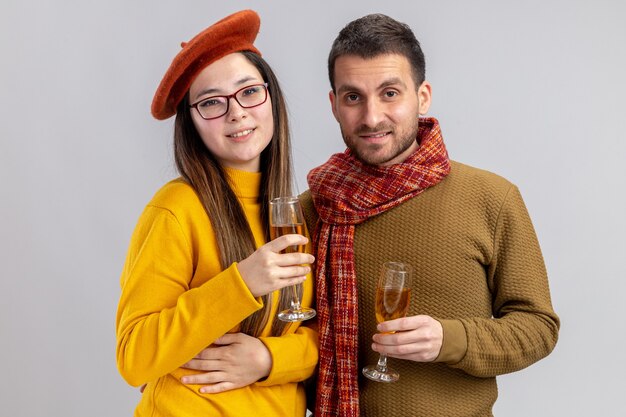 молодая красивая пара счастливый мужчина и улыбающаяся женщина в берете с бокалами шампанского, весело улыбаясь в любви вместе, празднуя день святого валентина, стоя на белом фоне