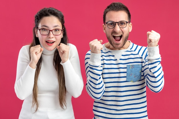 young beautiful couple happy man and woman in casual clothes wearing glasses  happy and excited clenching fists celebrating valentines day concept standing over pink wall