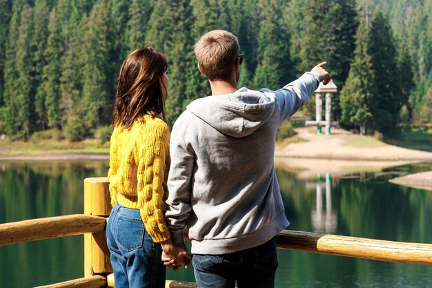 Young beautiful couple holding hands, enjoying mountains lanscape near lake