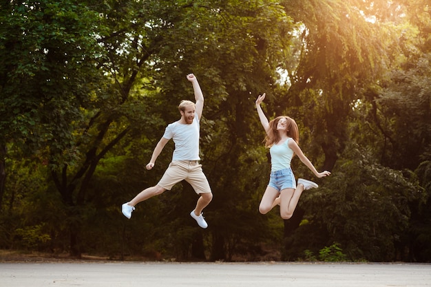 Young beautiful couple jumping, smiling, rejoicing, walking in park.