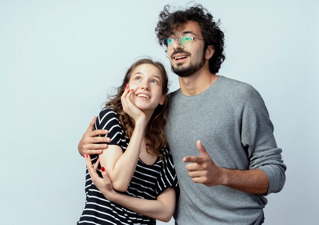 young beautiful couple man hugging his beloved girlfriend happy in love looking aside standing over white wall