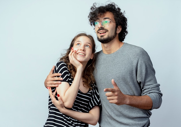 young beautiful couple man hugging his beloved girlfriend happy in love looking aside standing over white wall