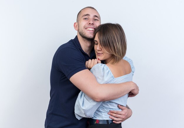 Young beautiful couple man and woman embracing happy in love together smiling cheerfully standing over white wall