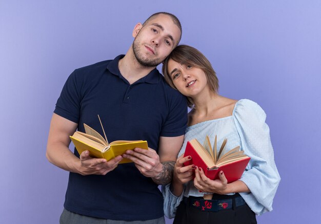 Young beautiful couple man and woman holding books in hands happy and positive smiling cheerfully standing