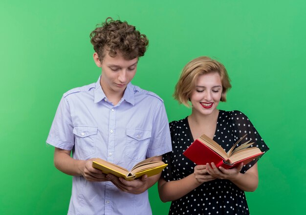 緑の壁の上に立っている顔に笑顔でそれらを見て本を保持している若い美しいカップルの男性と女性