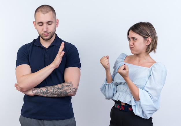 Young beautiful couple man and woman quarreling angry woman looking at her boyfriend who makes stop gesture with hand standing