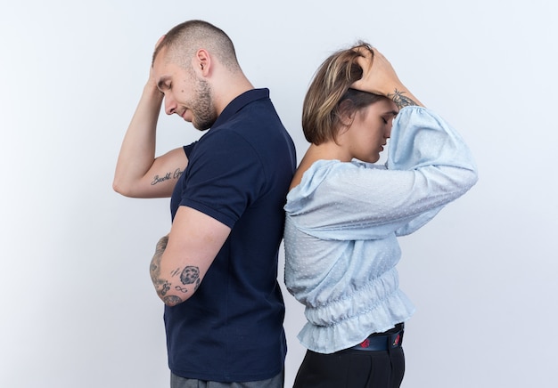 Young beautiful couple man and woman quarreling standing back to back over white wall