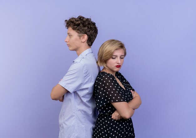 青い壁の上に立って眉をひそめている若い美しいカップルの男性と女性
