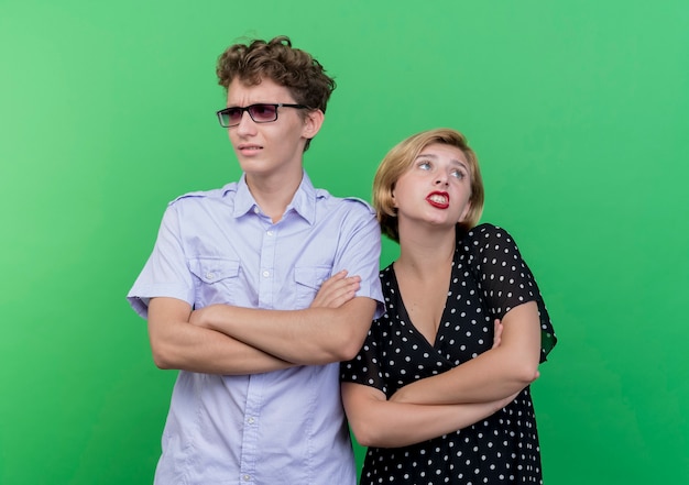 Young beautiful couple man and woman standing next to each other looking confused standing over green wall