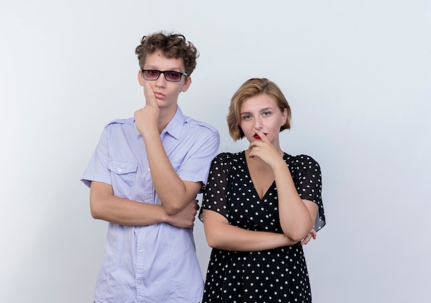 Young beautiful couple man and woman standing next to each other  with pensinve expression over white wall