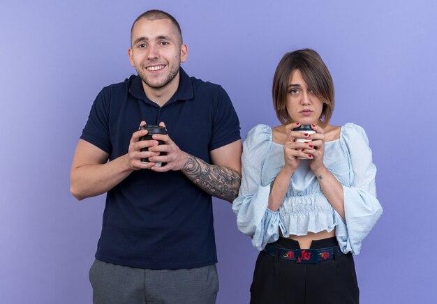 Young beautiful couple man and woman with paper cups looking happy and positive smiling standing