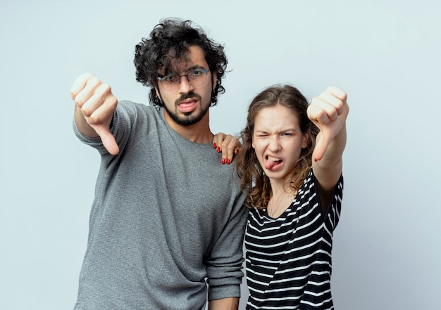 Free photo young beautiful couple man and women  displeased showing thumbs down over white wall