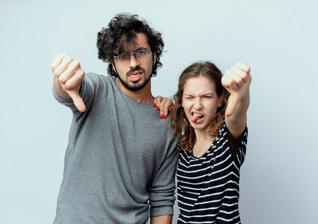 Young beautiful couple man and women looking at camera displeased showing thumbs down over white background