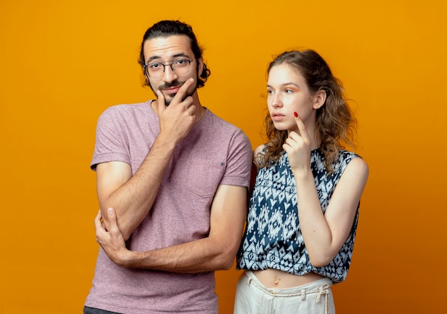 Free photo young beautiful couple man and women looking puzzled thinking standing over orange wall