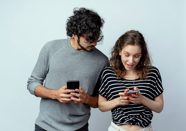 若い美しいカップルの男性と女性、白い壁を越えて彼のガールフレンドの携帯電話をスパイして覗く男