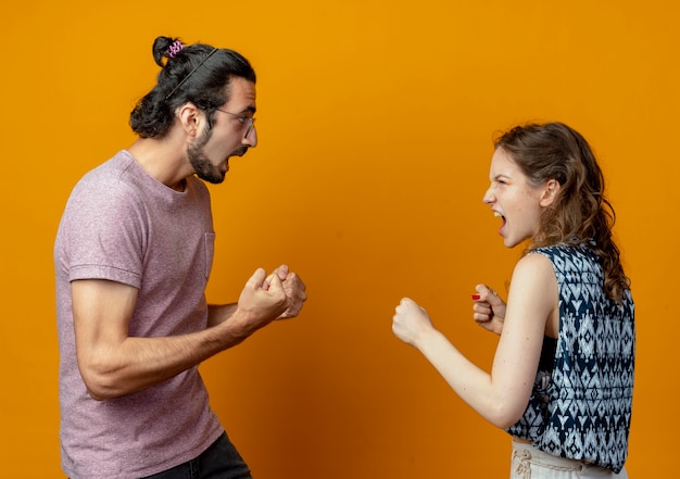 Young beautiful couple man and women quarreling and gesturing having fight crazy and frustrated standing over orange wall