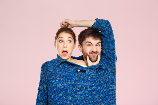 Free photo young beautiful couple in one blue knitted sweater posing smiling having fun over light pink wall