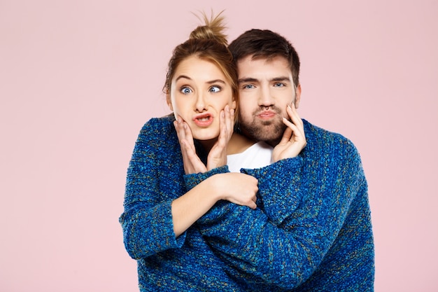 Free photo young beautiful couple in one blue knitted sweater posing smiling having fun over light pink wall