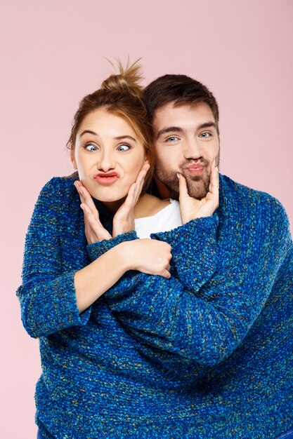 Young beautiful couple in one blue knitted sweater posing smiling having fun over light pink wall