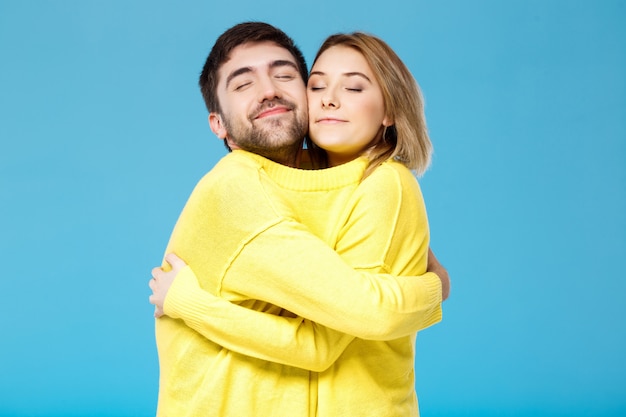 Young beautiful couple in one yellow sweater embracing over blue wall
