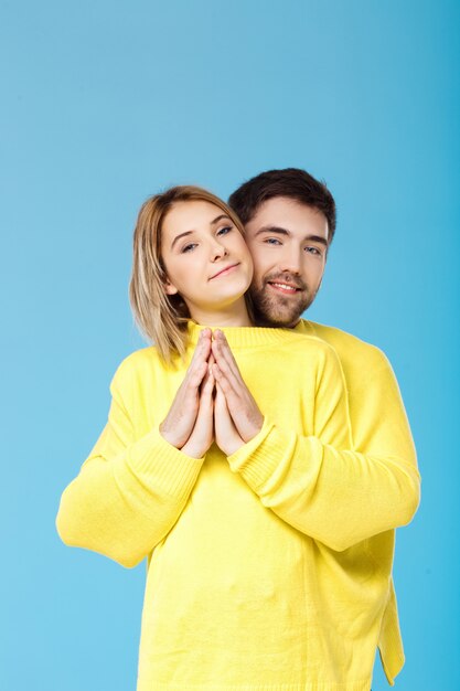 Young beautiful couple in one yellow sweater embracing smiling over blue wall