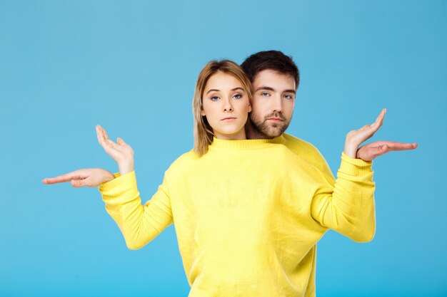 Young beautiful couple in one yellow sweater posing smiling having fun over blue wall
