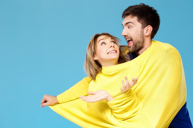 Young beautiful couple in one yellow sweater posing smiling having fun over blue wall