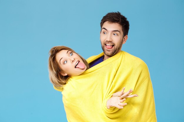 青で楽しんで笑ってポーズをとる1つの黄色いセーターの若い美しいカップル