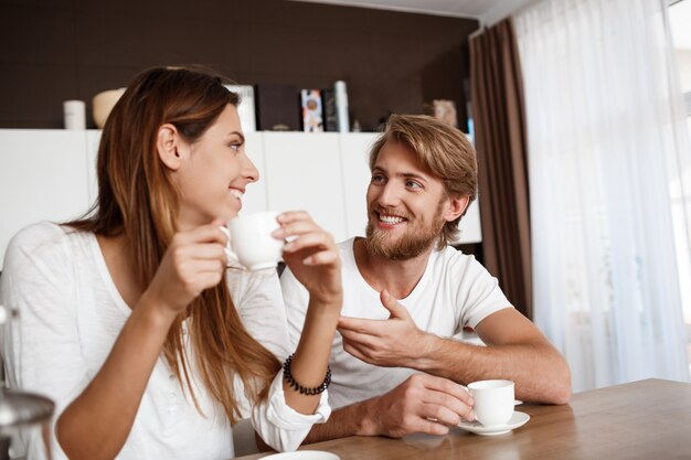 Young beautiful couple sitting at kitchen drinking morning coffee smiling.