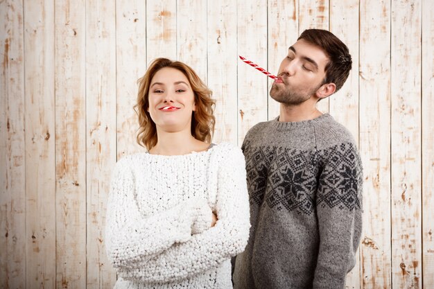Молодая красивая пара, улыбаясь, едят рождественские конфеты над деревянной стеной