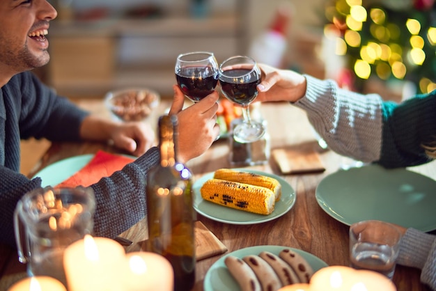 無料写真 幸せで自信を持って微笑む若い美しいカップル自宅でクリスマスを祝う食べ物を食べ、ワインのカップで乾杯