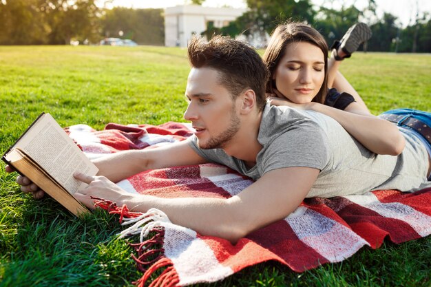 Young beautiful couple smiling reading at park.