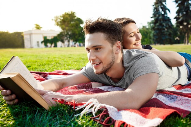 Young beautiful couple smiling reading at park.