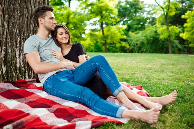 Young beautiful couple smiling, resting on picnic in park.