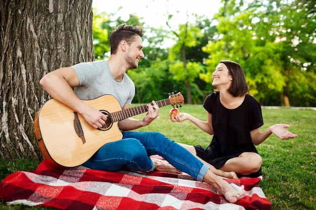 Young beautiful couple smiling, resting on picnic in park.